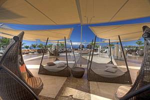 Gran Melia Palacio de Isora Loungebereich mit hängenden Sonnenschirmen und Liegen.