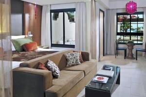 Innenansicht einer Hotelsuite im Gran Melia Palacio de Isora mit großem Bett, Sofa, Tisch, und Fenstern.