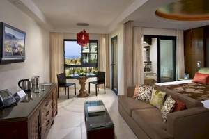 Innenansicht einer Suite im Gran Melia Palacio de Isora Hotel mit Bett, Couch, Tisch und Fernseher.