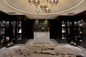 Innenbereich des Hyatt Place Taghazout Bay Hotels mit schwarzen Wänden, Marmorrezeption, hängenden Kronleuchtern und verschiedenen Regalen mit Produkten.