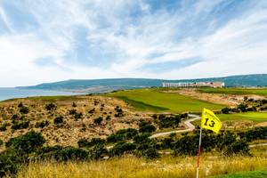 Golfplatz mit Blick auf das Meer und das Hyatt Place Taghazout Bay Hotel in der Ferne.
