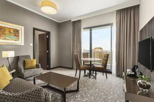 Wohnzimmer im Hawthorn Suites Abu Dhabi mit grauem Teppich, Sofa, Couchtisch, Esstisch und Fernseher.