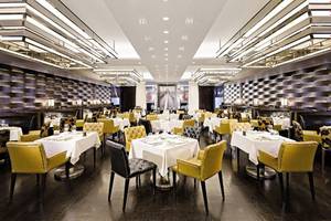 Innenansicht eines Restaurants im Jumeirah Emirates Towers mit gelben und schwarzen Stühlen und weißen Tischen.