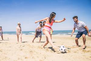 Gruppe von Menschen, die Fußball auf dem Strand spielen, bei klarem Himmel.