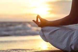 Person in Yoga Meditation am Strand bei Sonnenuntergang