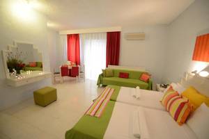 Innenansicht eines Zimmers im Golden Star Hotel auf Kos mit zwei Betten, grünen Kissen und einem grünen Sofa.