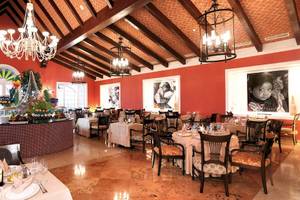 Innenbereich des Restaurants im Barcelo Maya Palace Hotel mit roten Wänden, Tischdecken und Kronleuchtern.