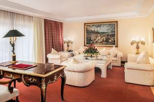 Luxuriöses Hotelzimmer mit einem Arbeitstisch, Sofas, Lampen und einem großen Gemälde an der Wand.