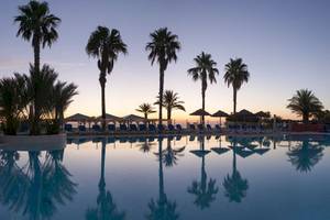 Sonnenuntergang am Pool des Belambra Clubs Pineto mit Palmen und Sonnenliegen.