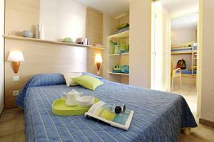 Ein geräumiges Zimmer im Belambra Clubs Pineto mit einem Bett, Büchern, einem Tisch und einer Lampe.