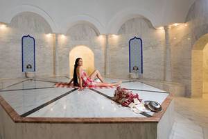 Eine Frau sitzt in einem weißen Saunabereich des Melas Lara Hotels, umgeben von Marmorwänden und blauen Verzierungen.