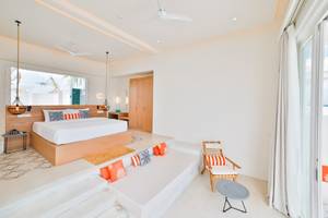 Modernes Zimmer im Sun Siyam Iru Veli Hotel mit großem Bett, Kissen und Holzmöbeln.
