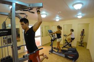 Fitnessstudio im ROC Arenas Doradas Hotel mit drei Personen, die an verschiedenen Geräten trainieren.