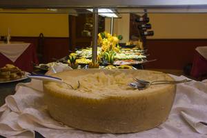 Ein großer Käse wird auf einem Tisch serviert, während hinter ihm ein Buffet mit verschiedenen Gerichten zu sehen ist.