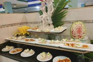 Foto des Speisenbuffets im ROC Arenas Doradas Hotel, mit verschiedenen Gerichten und einer Wassermelonenskulptur.