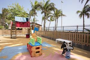 Spielplatz im Hipotels La Geria mit bunten Spielgeräten und einem Blick auf den Strand.