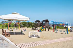 Kinderspielplatz am Strand des Mastichari Bay Hotels mit bunten Schaukeln und Geräten.