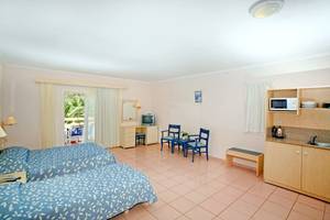 Doppelzimmer im Mastichari Bay Hotel mit zwei Betten, Schreibtisch, Fernseher, Stühlen und Küche.