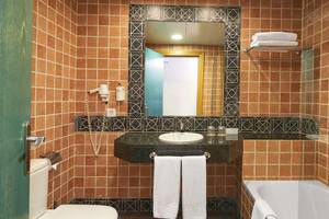 Badezimmer im Sol Barbados Hotel mit braunen Fliesen, einem Waschbecken, einem Spiegel und einer Badewanne.