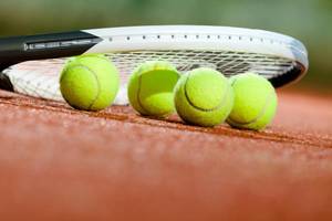 Tennisschläger und Tennisbälle auf einem roten Tennisplatz.