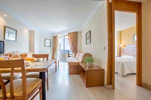 Innenansicht eines Zimmers im Hipotels Bahia Grande Hotel mit Esstisch, Sofa und Bett.
