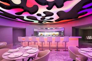 Hotel-Bar-Lounge-Bereich mit Tisch, Barhockern und violett-pinker Beleuchtung.