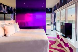 Schlafzimmer im Temptation Cancun Resort mit violetter Wand, Fernseher und Fenstern.
