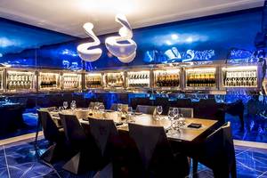 Innenbereich des Temptation Cancun Resort Restaurants mit langem Tisch, blauen Wänden und Flaschen im Kühlschrank.
