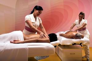 Zwei Frauen im Temptation Cancun Resort geben Massagen an zwei Gästen auf Massagetischen.