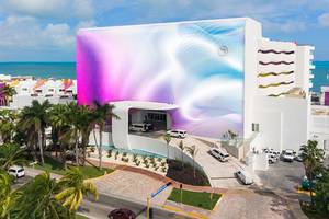 Außenansicht des Temptation Cancun Resorts mit einer großen Wandgestaltung und mehreren Fahrzeugen vor dem Gebäude.