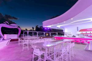 Loungebereich des Temptation Cancun Resorts bei Nacht mit pinker Beleuchtung und Tischen.