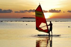 Windsurfer auf einem Segelbrett am Sonnenuntergang im Meer.