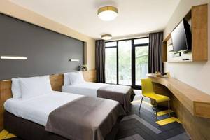 Zwei Doppelbetten mit weißen Kissen und grauen Decken in einem modernen Hotelzimmer.
