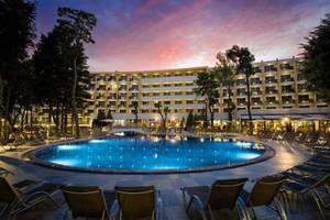Der Poolbereich des HVD Club Bor Hotels bei Sonnenuntergang mit vielen Liegen und Bäumen.