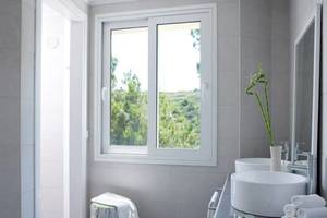 Badezimmer im Proteas Blu Resort mit zwei Waschbecken, einer Dusche und Fenster mit Blick auf die Landschaft.
