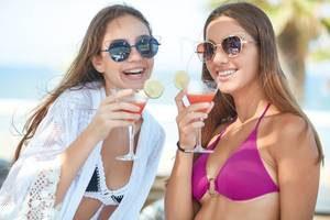 Zwei Frauen am Strand, die Cocktails mit Zitronenscheiben genießen.