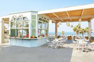 Außenbereich des Grecotel Olympia Oasis Aqua Park mit Terrasse, Tischen und Stühlen.