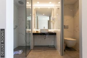 Badezimmer im Aphrodite Beach Club Deluxe Room mit Glasdusche, Waschbecken und Toilette.