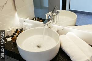 Ein Deluxe Badezimmer im Aphrodite Beach Club mit einem Waschbecken, das Wasser fließt, und Handtüchern.