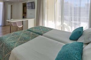 Innenansicht eines Zimmers im BQ Apolo Hotel mit zwei Betten, Tisch, Fernseher und Balkon.