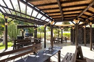 Gartenrestaurant im Barcelo Margaritas Hotel mit hölzernen Tischen und Bänken unter einem Strohdach.