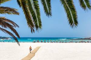 Strand des Barcelo Fuerteventura Mar mit Palmen und einem Mann, der auf dem Steg geht.