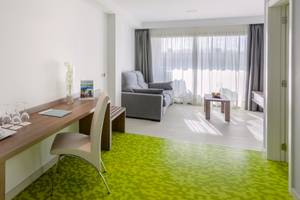Innenansicht eines Zimmers im Barcelo Fuerteventura Mar Hotel mit Schreibtisch, Stuhl, Couch und Fenstern.