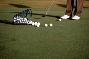 Golfplatz mit Golfer, Golfschläger, Golfbällen und Golfkorb.