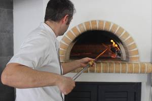 Ein Koch im Blue Aegean Hotel & Suites benutzt einen langen Holzstab, um Pizza im Ofen zu backen.