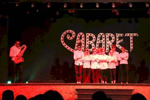 Aufführung eines Cabarets mit einem Musiker und Schauspielern auf der Bühne.