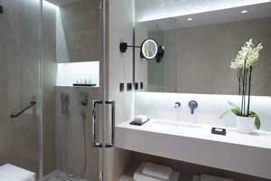 Badezimmer im Neptune Luxury Resort mit Glasdusche, Waschbecken, Spiegel und Blumenvase