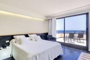Hotelzimmer mit Balkon und Meerblick, Bett und Kissen, Stühle und Tisch draußen