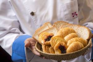 Ein Mitarbeiter des Beyond Resort Krabi hält eine Schale mit Croissants und Brötchen.