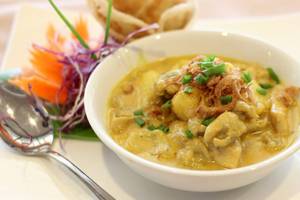 Ein weißer Bowl mit gelber Currysuppe, serviert mit einem Löffel und Beilagen, im Hotel Beyond Resort Krabi.